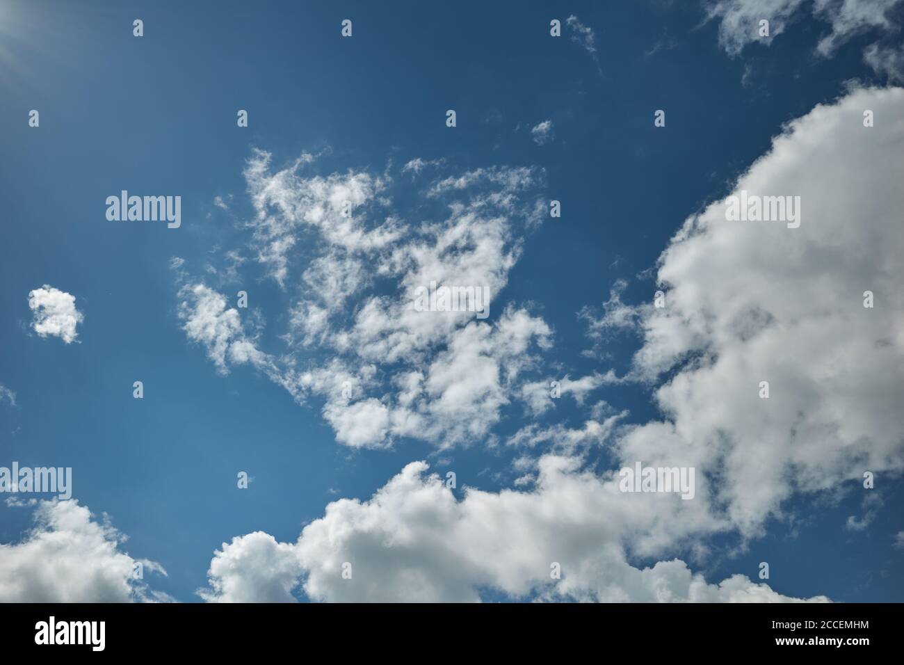 Azure sky with clouds lit by bright sun. The sun`s rays lit up a blue heaven covered with clouds. Background for forecast and meteorology illustration Stock Photo